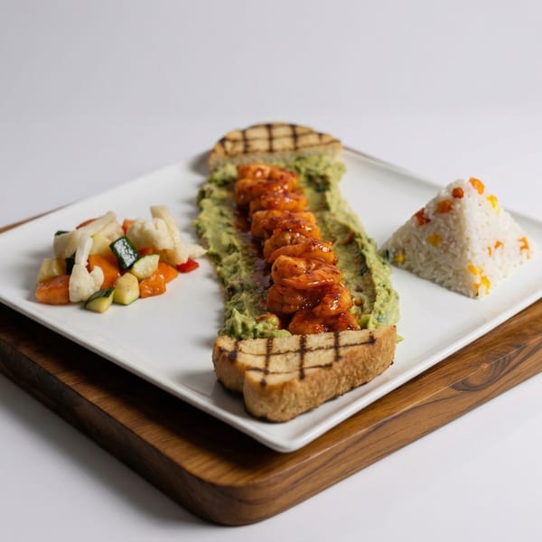 Grilled shrimp on guacamole toast with a side of mixed vegetables and pyramid-shaped rice.