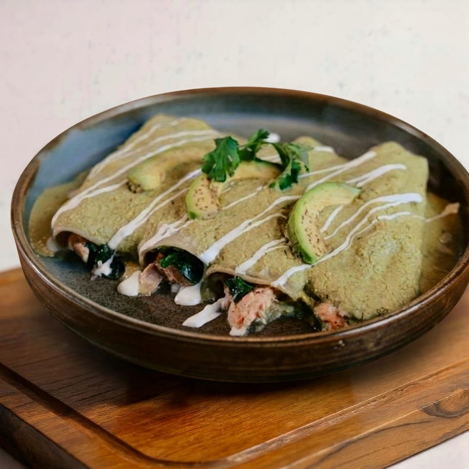 Three enchiladas verdes with chicken, spinach, avocado slices, and crema in a rustic bowl.